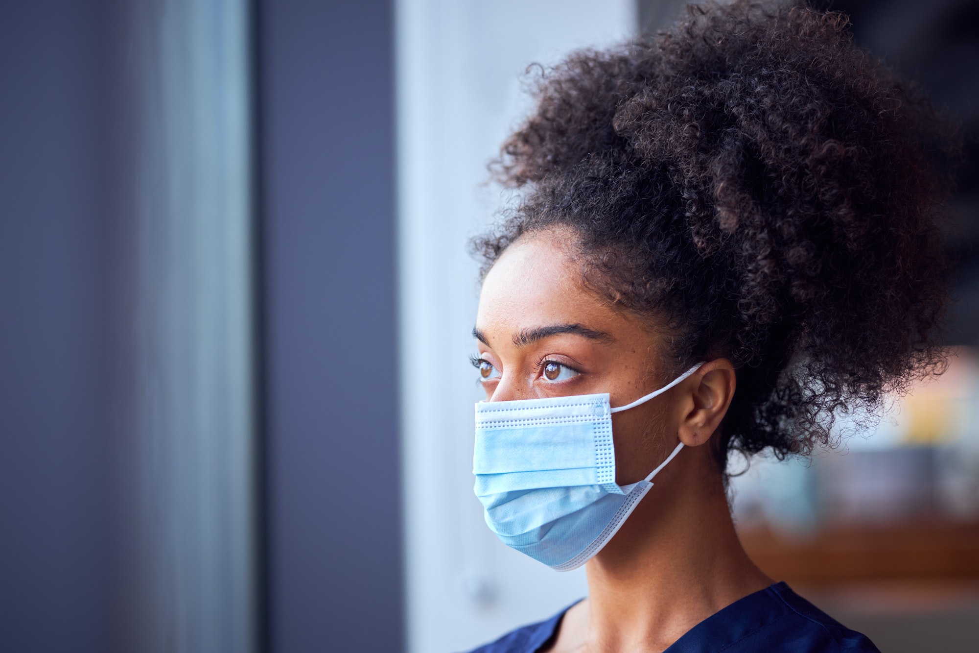 Female Doctor In Face Mask Wearing Scrubs Under Pressure In Busy Hospital During Health Pandemic